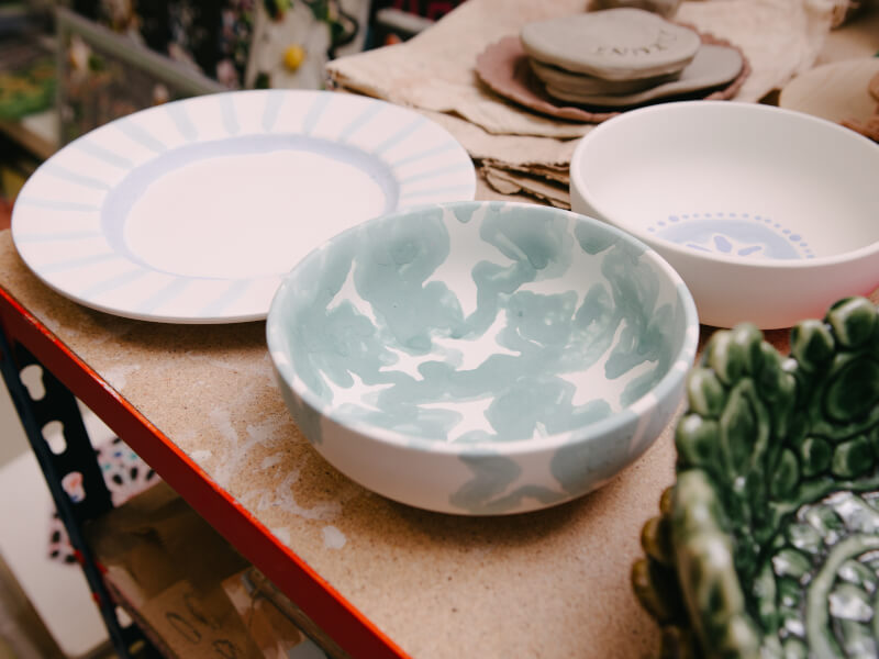 Two hand-painted ceramic bowls and a plate on a bench